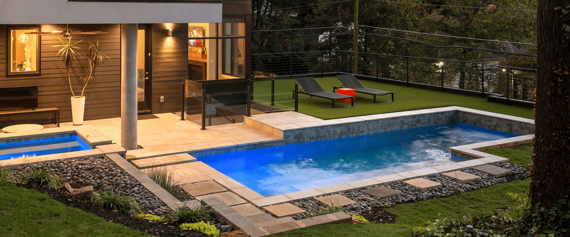 Modern backyard swimming pool with blue underwater lighting, raised spa, and sun loungers on a custom patio.