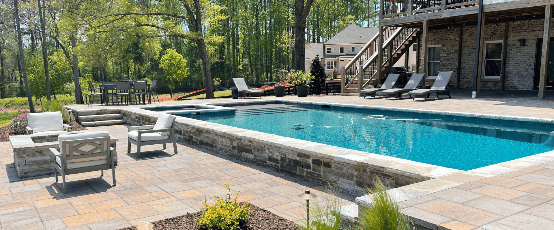 Luxury outdoor swimming pool design featuring a built-in spa, stone patio, and fire pit seating area.