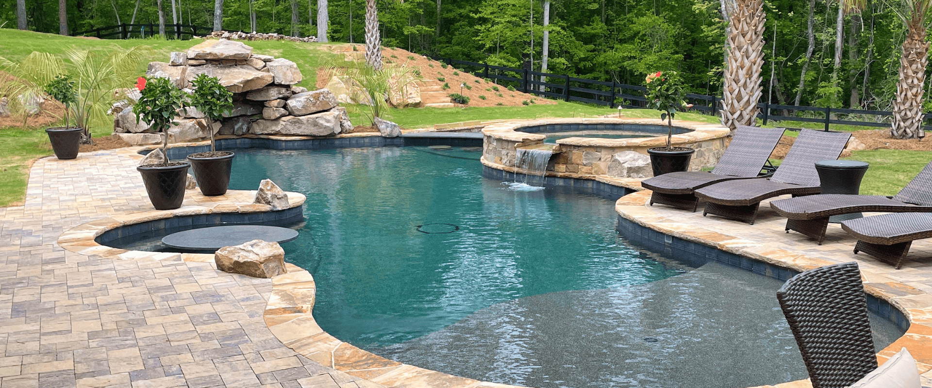 rcsseptblog1 Custom freeform pool featuring a rock waterfall, raised spa, tanning ledge, and paver patio on an estate-style property.